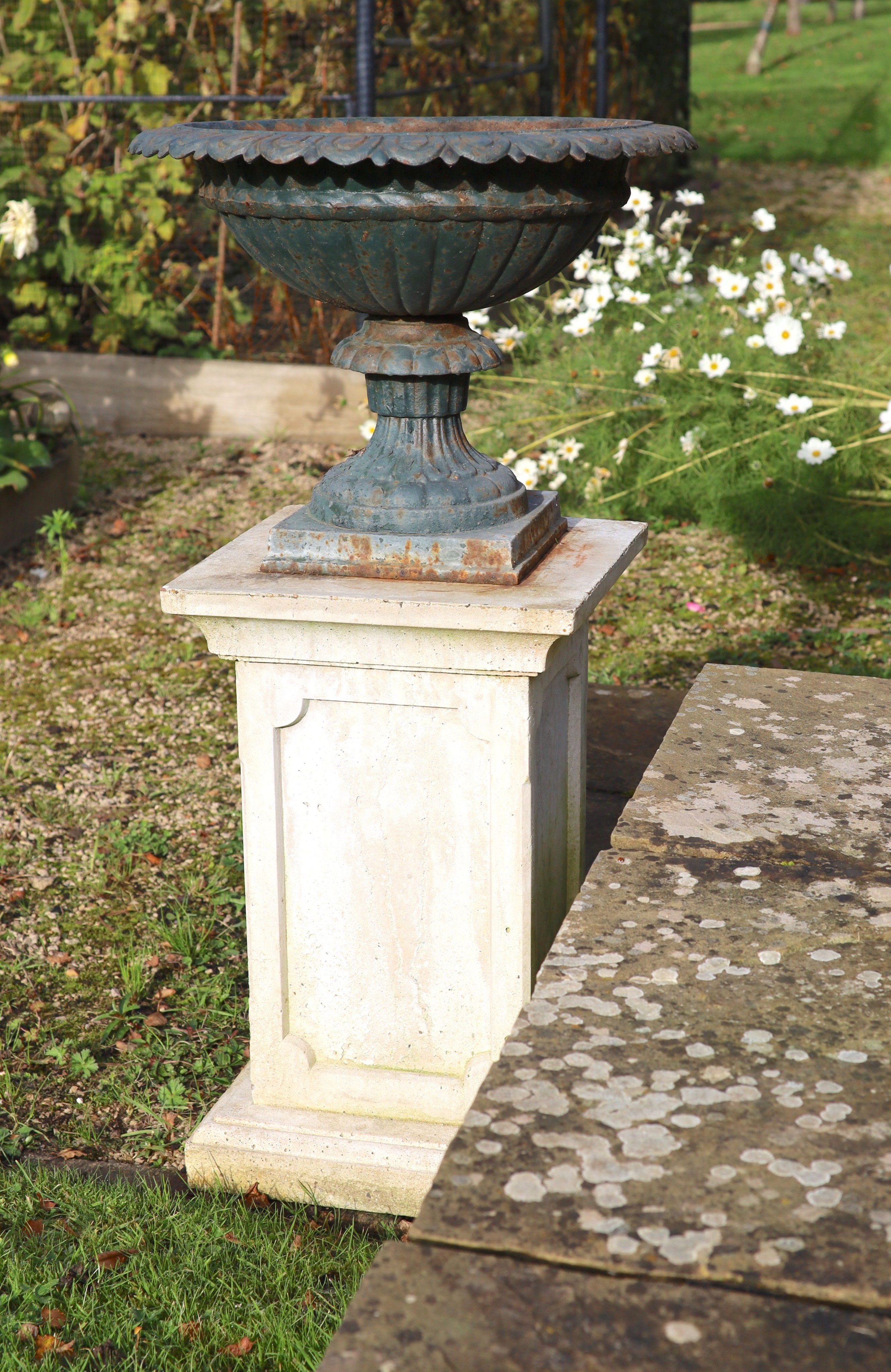 A pair of green painted cast iron garden urns on reconstituted stone pedestals, diameter 52cm height 99cm